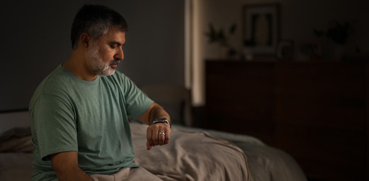 En man sitter i en säng och tittar på sin Apple Watch.